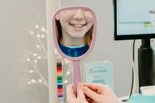 Smiling patient with braces looking into a handheld mirror during an orthodontic visit, representing braces care and treatment guidance at Griffin Orthodontics, Vernon, CT 06066.