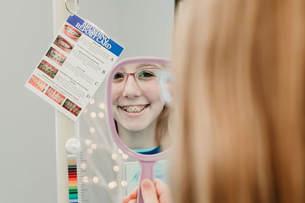 Smiling patient looking into an orthodontic mirror while reviewing treatment information, representing real smile transformations and personalized orthodontic care at Griffin Orthodontics, Vernon, CT 06066.