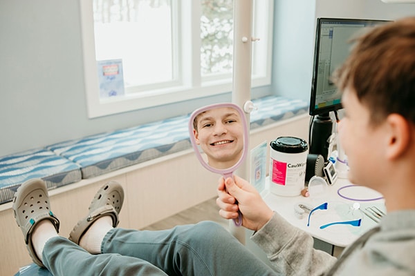 Patient smiling into a handheld mirror during an orthodontic visit, representing clear aligner treatment cost and personalized smile investment at Griffin Orthodontics, Vernon, CT 06066.