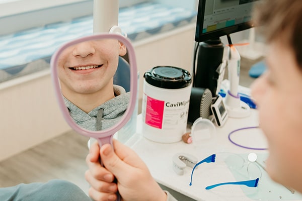 Orthodontic patient smiling into a handheld mirror after treatment, representing retainer guidance and long-term smile maintenance at Griffin Orthodontics, Vernon, CT 06066.
