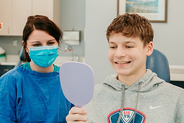 Teen patient smiling while looking into a handheld mirror during an orthodontic visit, representing personalized teen orthodontic treatment at Griffin Orthodontics, Vernon, CT 06066.