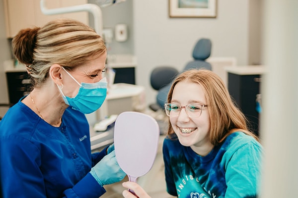 Orthodontic team member helping a smiling patient view her teeth with a handheld mirror, representing modern braces and personalized treatment options at Griffin Orthodontics, Vernon, CT 06066.