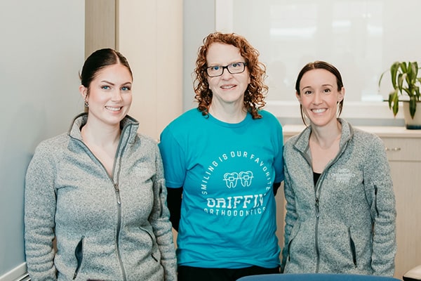 Three Griffin Orthodontics team members smiling together in a bright office space, representing a welcoming and supportive orthodontic care team at Griffin Orthodontics, Vernon, CT 06066.