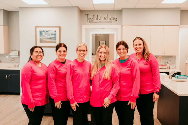Team members smiling together in a bright, welcoming orthodontic practice, wearing matching pink uniforms at Griffin Orthodontics, Vernon, CT 06066.